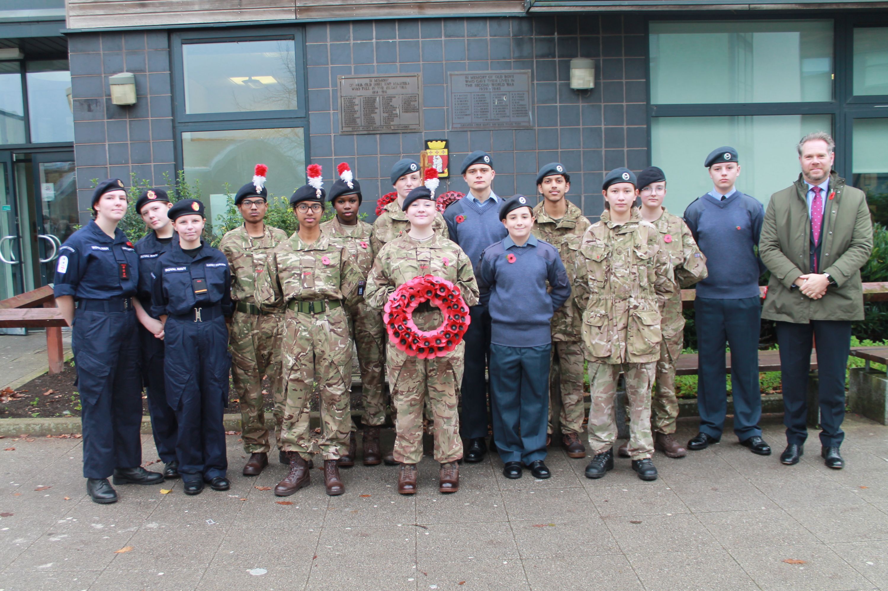 14 students in their cadet uniforms with the Head Teacher holding a wreath to be laid at the ceremony 